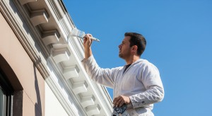Painter detailing fascia trim on home under clear blue sky