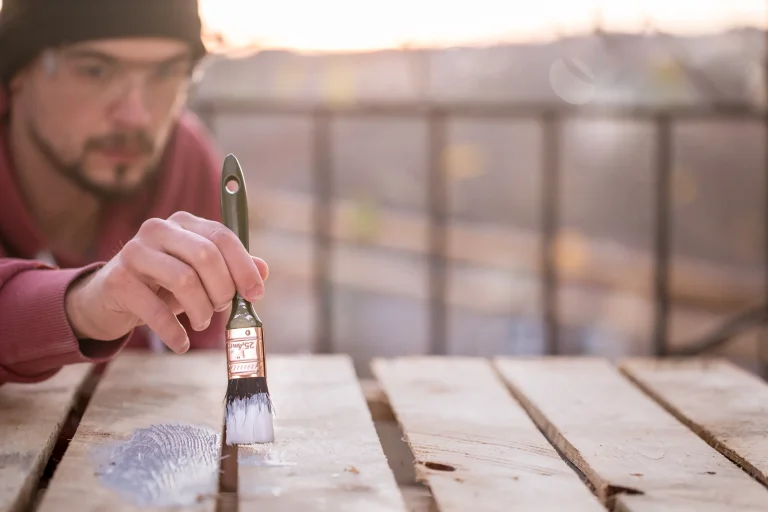 A man applies paint to a wooden surface while concentrating intently