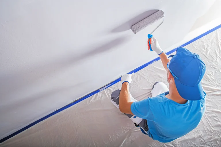 A person in a blue shirt applies paint to a wall using a roller