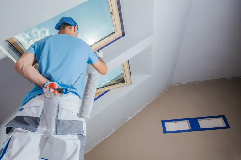 A painter applies finishing touches to a ceiling near a skylight