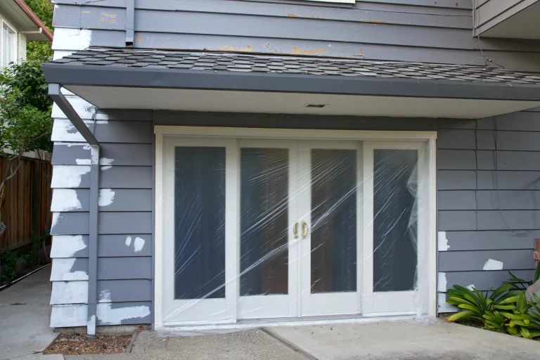 A set of white double doors is covered by plastic sheeting near a partially painted gray wall