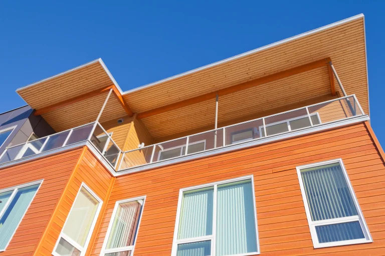 A modern orange building features a balcony and large windows against a clear blue sky
