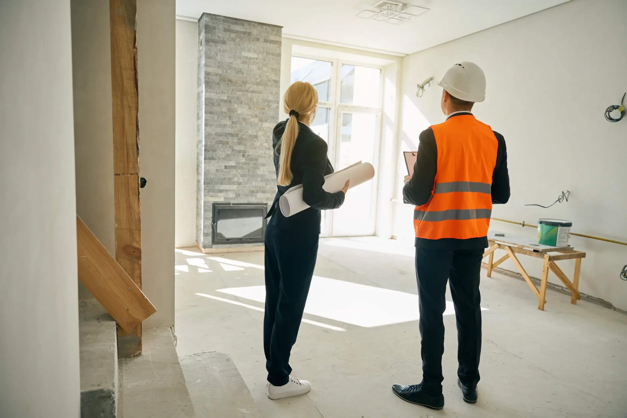 A construction worker and an architect discuss plans in a partially finished room