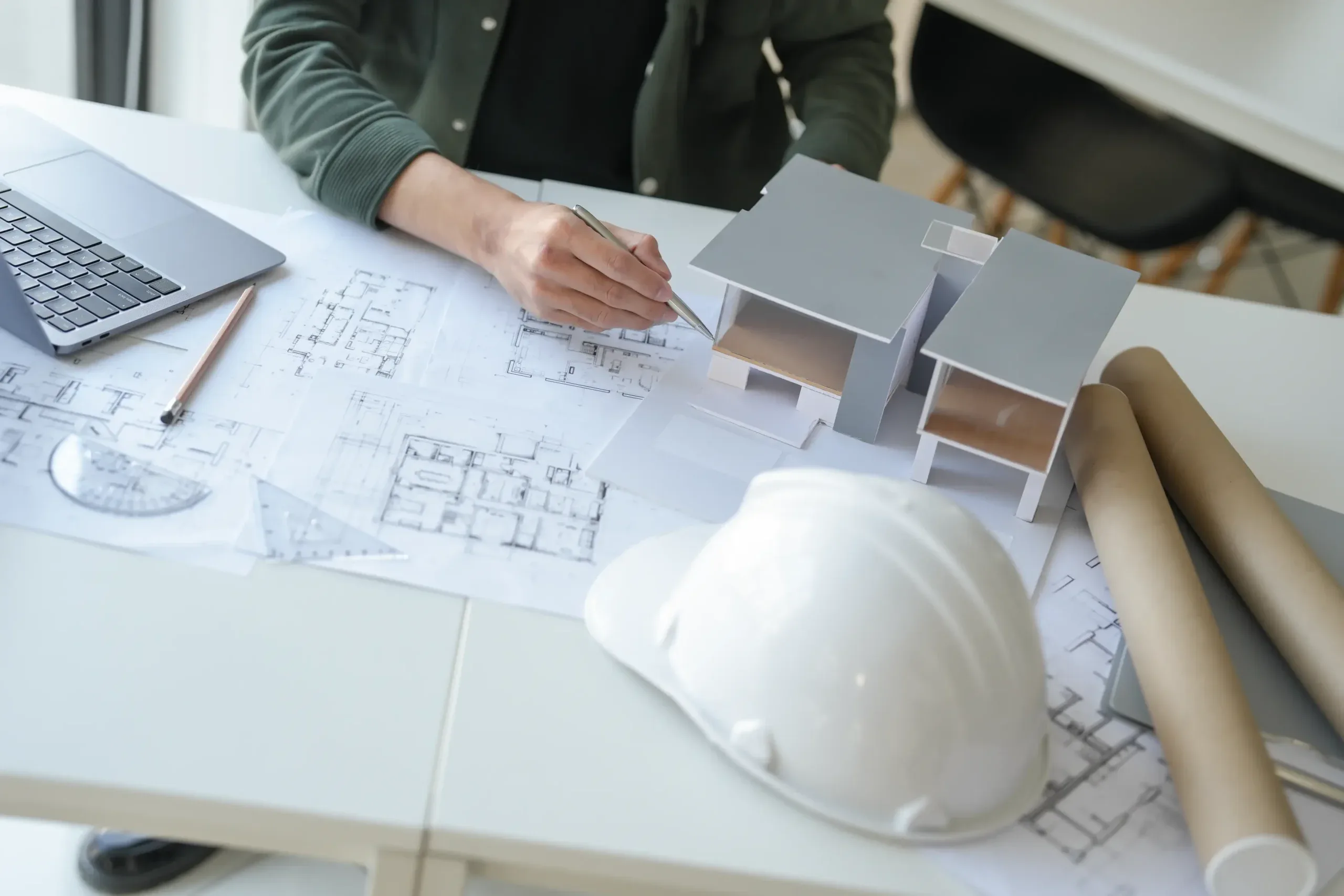 A person examines architectural blueprints while working on a model building