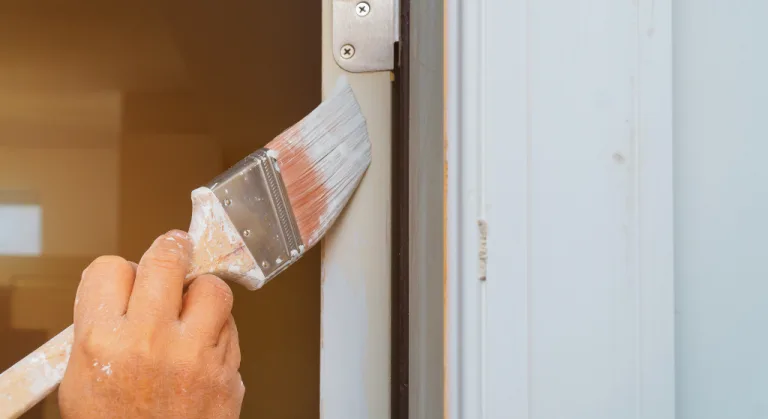 A hand is painting a doorframe with a brush