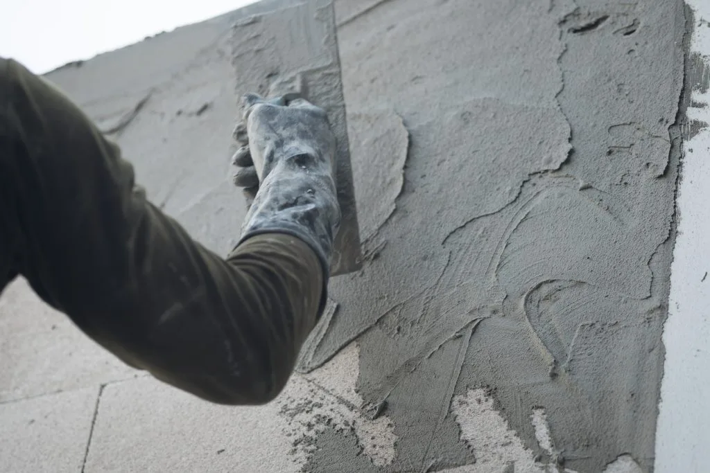 Airdrie worker applying wet cement to a wall with a trowel